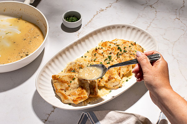 seasoned lightly breaded chicken breasts on oval platter, butter sauce being spooned over