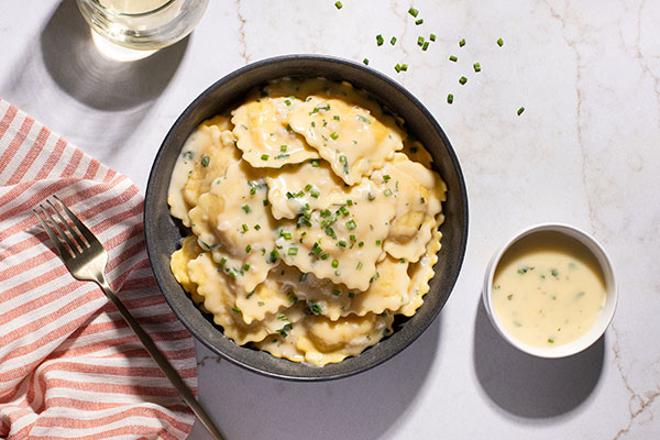 bowl of ravioli with butter sauce and chopped chives, napkin, butter sauce, and beverage alongside