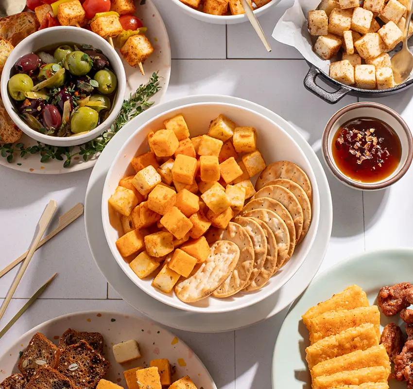 seasoned cheese cubes in bowl with crackers, surrounded by other cheese-and-cracker type snacks