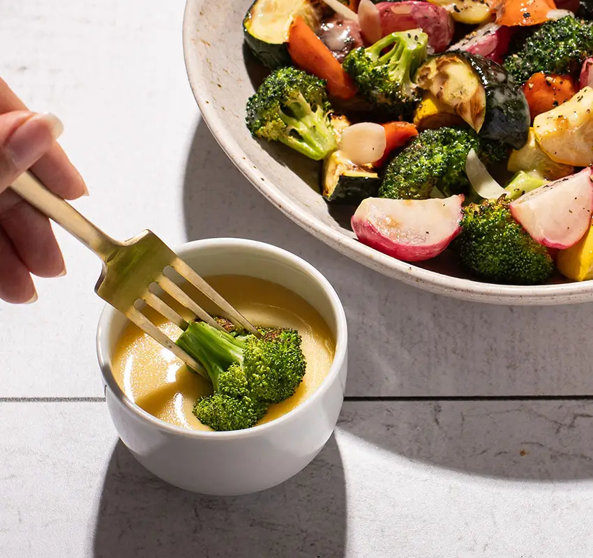 vegetables in a bowl with butter dipping sauce on the side, piece of broccoli being dipped on a fork
