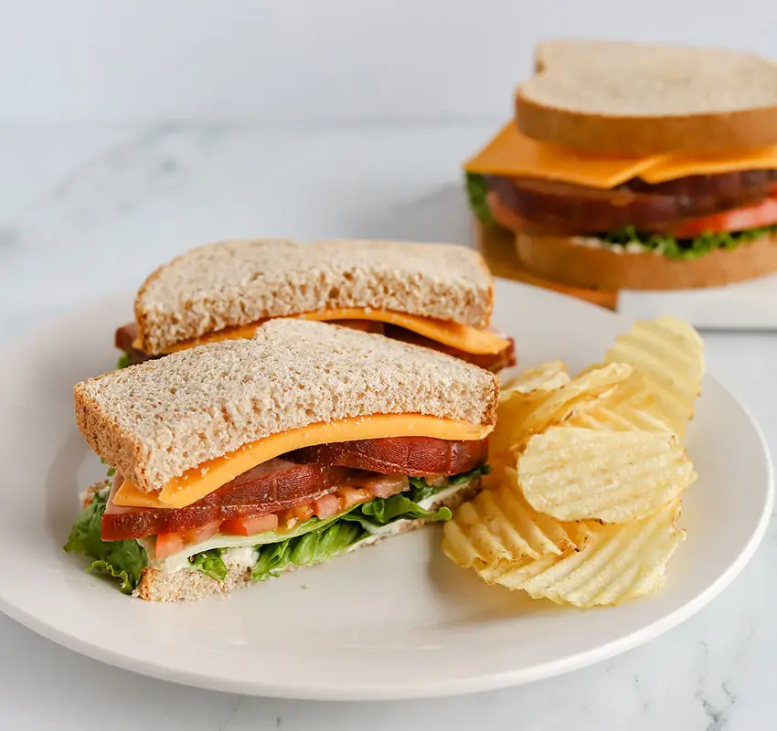 ham and cheese sandwich half on plate along with ripple chips