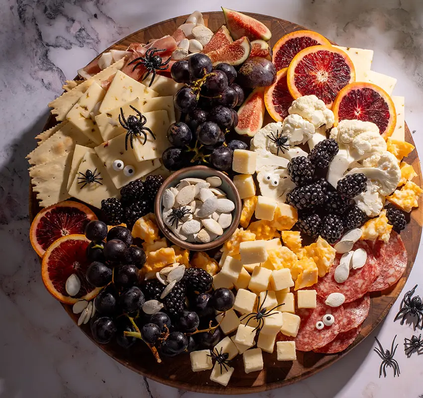 charcuterie board with meats, cheeses and fruit--googly eyes and plastic spiders added to make it spooky