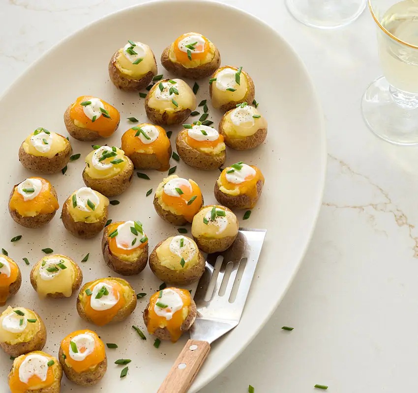 mini stuffed potato bites on serving platter along with serving spatula, all flecked with minced chives