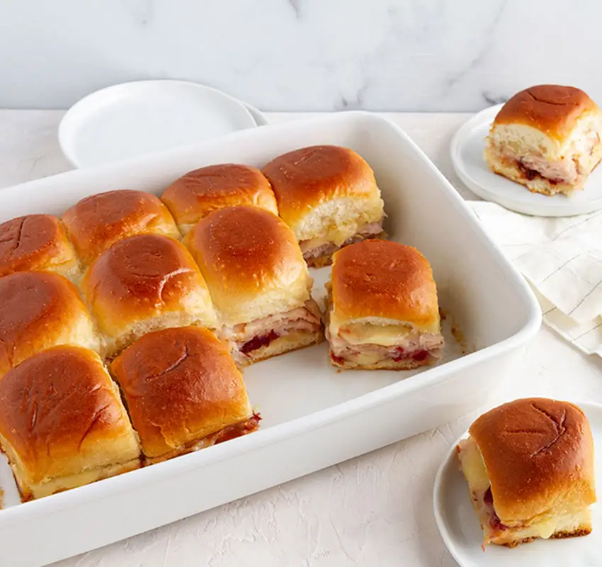 ceramic baking pan of party sandwiches, one hand lifting one sandwich out - 2 individual sandwiches on plates
